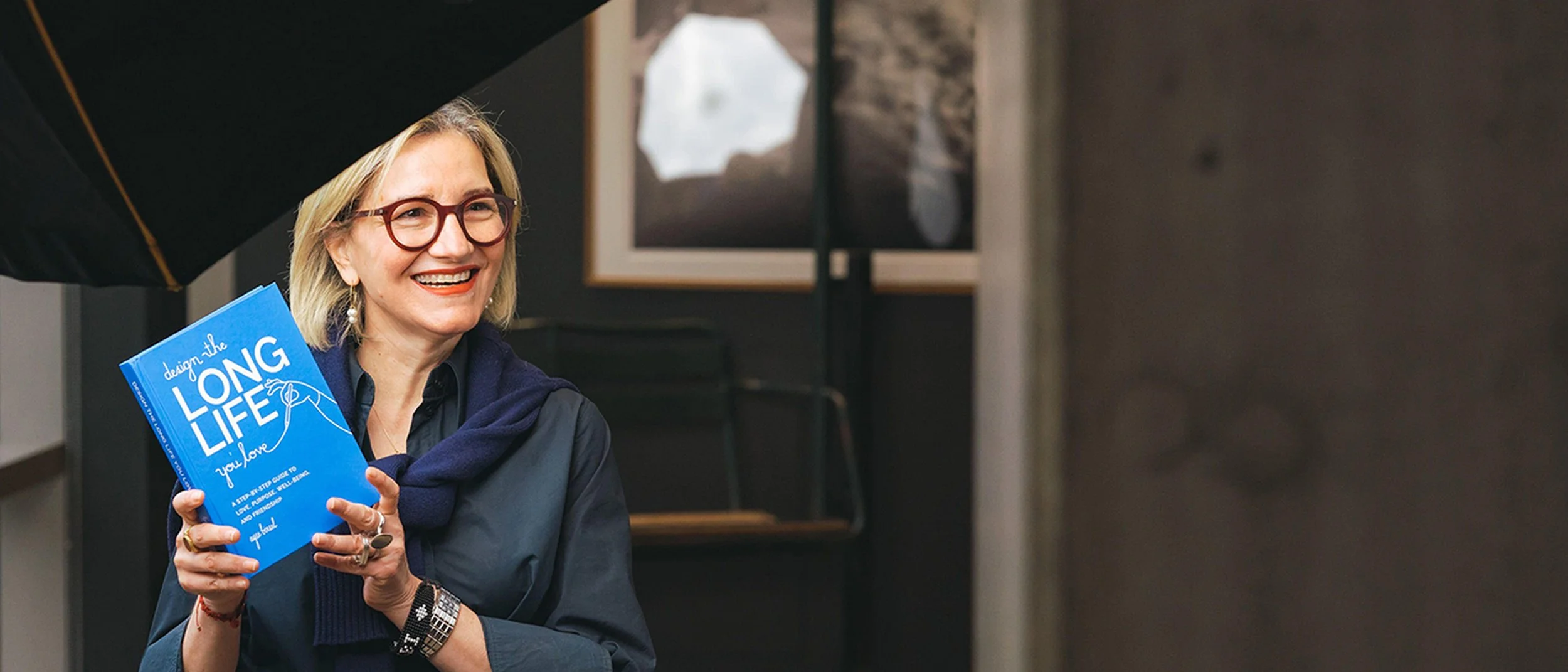 Ayse Birsel smiling, holding her book Design the LONG Life You Love